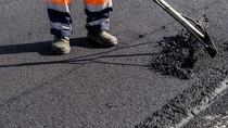 Worker in orange safety gear smooths fresh asphalt with a tool on a road. Worker in orange safety gear smooths fresh asphalt with a tool on a road.