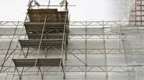 Scaffolding is set against a weathered concrete wall with visible metal reinforcements and patches, conveying a sense of ongoing repair or construction. Scaffolding is set against a weathered concrete wall with visible metal reinforcements and patches, conveying a sense of ongoing repair or construction.