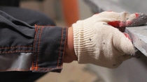 A worker wearing white gloves and a dark jacket installing a metal strip. A worker wearing white gloves and a dark jacket installing a metal strip.