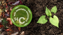 The picture you described shows a close-up view of soil with a small green plant growing on the right side. On the left side, there is a mixture of organic matter such as decomposing leaves and vegetable scraps, partially covered by soil. Overlaid on this part of the image is a circular graphic containing the text "with detectable biocontent 14C."