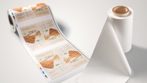 A roll of printed packaging design for cereal bars unrolls, displaying multiple labels with text and cereal imagery.