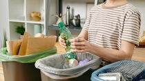 A woman recycles different packaging into different trash cans. 