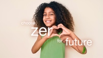 Smiling child with curly hair in a green dress makes a heart shape with hands. Text overlay reads "choose zero for future" on a neutral background. Smiling child with curly hair in a green dress makes a heart shape with hands. Text overlay reads "choose zero for future" on a neutral background.