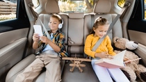 Smiling kids with smartphone and book sitting near toys on back seat of car . Smiling kids with smartphone and book sitting near toys on back seat of car .