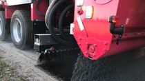 A red road paver machine lays gravel on a path, with its rear section visible.