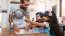 A girl and a boy are washing their hands in the kitchen while the father is watching. A girl and a boy are washing their hands in the kitchen while the father is watching.