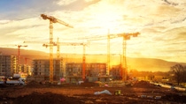 Large construction site including several cranes working on a building complex, illumined by warm gold sunlight. Large construction site including several cranes working on a building complex, illumined by warm gold sunlight.