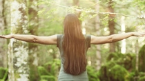 Woman with long hair spreading her arms in the forest, as seen from behind .