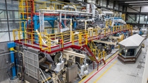 A large industrial machine (pilot coater) with yellow and red railings occupies a spacious factory floor.  A large industrial machine (pilot coater) with yellow and red railings occupies a spacious factory floor.
