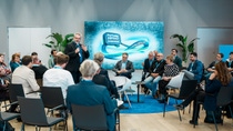 A diverse group of people in business attire engage in a discussion at a conference titled "Future Asphalt Symposium," set in a modern meeting room, D105 in Ludwigshafen.