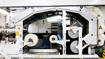 Large industrial pilot coater in a factory setting, with two rolls of paper loaded. The machine is white with exposed gears. Large industrial pilot coater in a factory setting, with two rolls of paper loaded. The machine is white with exposed gears.