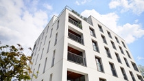 Modern white apartment building with multiple balconies and large windows, set against a bright blue sky with scattered clouds. Urban and serene. Modern white apartment building with multiple balconies and large windows, set against a bright blue sky with scattered clouds. Urban and serene.