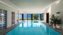 Indoor pool with clear blue water, surrounded by white walls and large floor-to-ceiling windows offering a scenic view of mountains and greenery.  Indoor pool with clear blue water, surrounded by white walls and large floor-to-ceiling windows offering a scenic view of mountains and greenery.