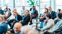 A diverse group of people seated in a bright conference room, smiling and engaging in discussion. 