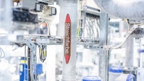 Industrial scene with a metal pipe labeled "Streichfarbe" in a factory setting, surrounded by wires and equipment.  Industrial scene with a metal pipe labeled "Streichfarbe" in a factory setting, surrounded by wires and equipment.