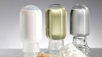 Three glass containers filled with white, yellow, and clear liquids are arranged on a reflective surface. The background is a soft gray gradient.