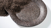 The photograph shows grained coffee which then, in the main focus, seems to morph into a plate made of coffee beans and coffee grain.