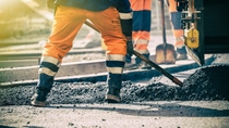 Workers in high-visibility clothing are paving a road with asphalt using shovels. Workers in high-visibility clothing are paving a road with asphalt using shovels.