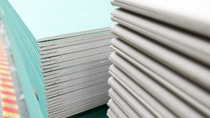 Stacks of light green and white drywall sheets are piled closely together, showcasing their layered edges. Stacks of light green and white drywall sheets are piled closely together, showcasing their layered edges.