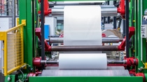 Industrial machine with green and red frame (Pilot coating center rewinder) rolling white fabric between metal rollers in a factory setting. Industrial machine with green and red frame (Pilot coating center rewinder) rolling white fabric between metal rollers in a factory setting.