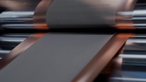 Close-up of a copper-colored metal sheet being rolled by sleek machinery. 
