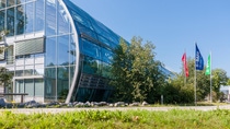 A glass-covered building of round shape with a green lawn and bright-colored BASF flags at the BASF site in Trostberg.  