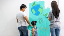 A family of three paints a wall teal with eco-friendly symbols, including Earth and recycling icons. A family of three paints a wall teal with eco-friendly symbols, including Earth and recycling icons.