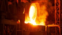 Molten metal pours from a large industrial crucible, glowing bright orange and surrounded by sparks and smoke in a dimly lit foundry. Molten metal pours from a large industrial crucible, glowing bright orange and surrounded by sparks and smoke in a dimly lit foundry.