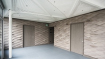 Modern room with textured beige walls and two closed doors. The ceiling is white with a geometric pattern, and the floor is light gray tile.
Inside the STEP2 unit of the NEST building: Two walls covered in wall panels of scale-like distribution and form, in light brown color. Credit: ROK Architekten Modern room with textured beige walls and two closed doors. The ceiling is white with a geometric pattern, and the floor is light gray tile.
Inside the STEP2 unit of the NEST building: Two walls covered in wall panels of scale-like distribution and form, in light brown color. Credit: ROK Architekten