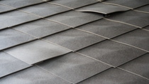 Close-up of a gray, slightly wavy tile roof showing overlapping, textured tiles.
Inside the STEP2 unit of the NEST building: Detail of wall panels, showing the unique 3D-formed scale-like design. Credit: ROK Architekten