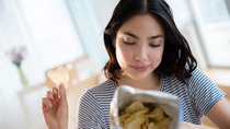 Hispanic woman reading ingredients on bag of potato chips