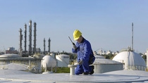 BASF tank storage facility in Ludwigshafen with industrial worker in safety gear performing inspection on a storage tank roof.