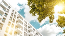 Modern white apartment building under a bright blue sky with fluffy clouds. Sunlight filters through green tree leaves,. Modern white apartment building under a bright blue sky with fluffy clouds. Sunlight filters through green tree leaves,.