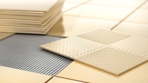 Close-up of beige and gray textured ceramic tiles. A stack of beige tiles is on the left, with one tile placed atop others on a grid-like layout. Close-up of beige and gray textured ceramic tiles. A stack of beige tiles is on the left, with one tile placed atop others on a grid-like layout.