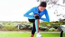 A woman in athletic wear stretches her leg on a park bench. She wears a blue jacket and black leggings in a green, scenic outdoor setting. A woman in athletic wear stretches her leg on a park bench. She wears a blue jacket and black leggings in a green, scenic outdoor setting.