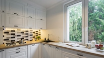 A bright kitchen with white cabinets, black and white tiled backsplash, and a wooden countertop. A window shows lush greenery. A bright kitchen with white cabinets, black and white tiled backsplash, and a wooden countertop. A window shows lush greenery.