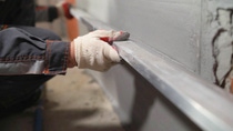 Close-up of a construction worker in white gloves smoothing a wall with a metal tool. Close-up of a construction worker in white gloves smoothing a wall with a metal tool.