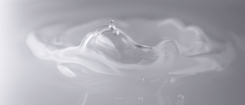 Close-up of a water droplet splashing into a smooth surface, forming ripples and a crown-like shape. Close-up of a water droplet splashing into a smooth surface, forming ripples and a crown-like shape.