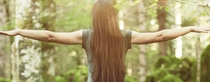 Woman with long hair spreading her arms in the forest, as seen from behind .