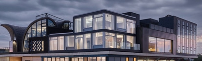 NEST innovation and research building in Dübendorf, Switzerland, featuring upcycling solutions. The image shows the STEP2 unit with lights on, contrasting a cloudy, dark sky. Credit: Zooey Braun