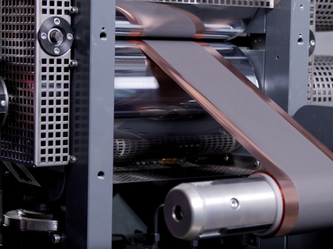 Close-up of an industrial machine with copper-colored film rolling through metal rollers. Close-up of an industrial machine with copper-colored film rolling through metal rollers.