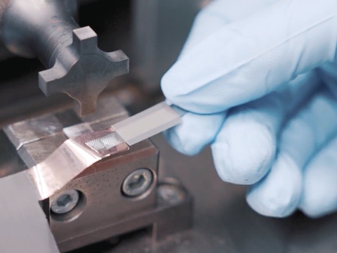 Gloved hands carefully position a metal piece on a machine, suggesting a precise manufacturing process. Gloved hands carefully position a metal piece on a machine, suggesting a precise manufacturing process.