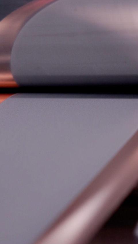 Close-up of industrial machinery featuring sleek, metallic rollers processing a flat, copper-colored sheet.
