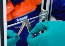 A person in a blue and orange uniform uses gloved hands to apply adhesive strips on a metal bar. A person in a blue and orange uniform uses gloved hands to apply adhesive strips on a metal bar.