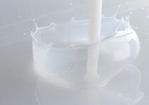 A stream of milky liquid splashes into a smooth, white surface, forming a circular crown with droplets suspended mid-air. A stream of milky liquid splashes into a smooth, white surface, forming a circular crown with droplets suspended mid-air.
