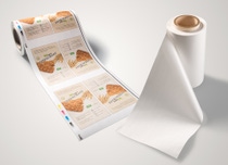 A roll of printed packaging design for cereal bars unrolls, displaying multiple labels with text and cereal imagery. A roll of printed packaging design for cereal bars unrolls, displaying multiple labels with text and cereal imagery.