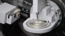 Automated laboratory analysis instrument examining a circular sample with precision probe in industrial testing.