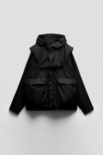Black puffer jacket hanging against a light gray background. Features a high collar, oversized front pockets, and a minimalist, stylish design. Black puffer jacket hanging against a light gray background. Features a high collar, oversized front pockets, and a minimalist, stylish design.