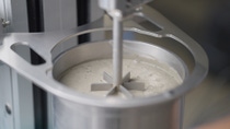 Industrial laboratory mixer stirring concrete slurry in a stainless steel vessel for materials testing.