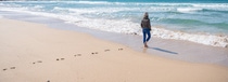 Woman leaving footprints on the beach, walking towards the water.